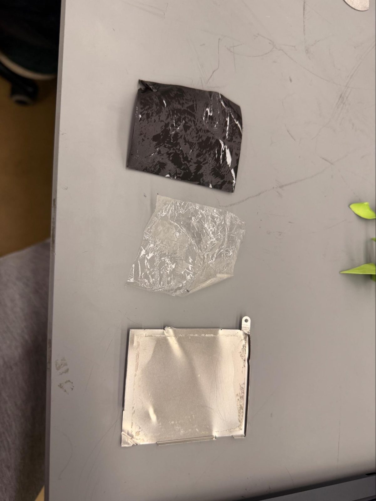 The black foam pad, the clear plastic film and the bare steel cover laid out separately