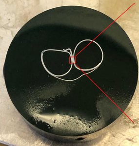 Black epoxy puck holding the cross-sectioned battery cover tab, with the tested area marked in red