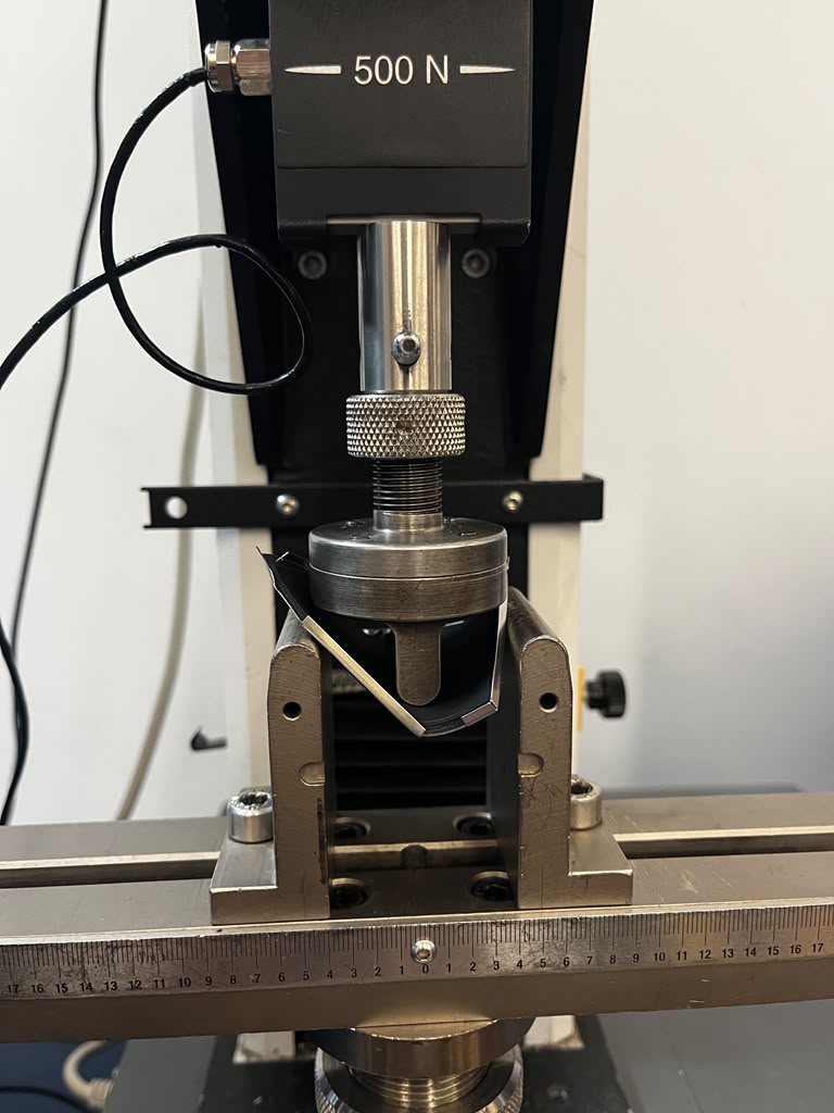 The same three-point bending fixture after the test, with the loading nose pressed down into the bent battery cover